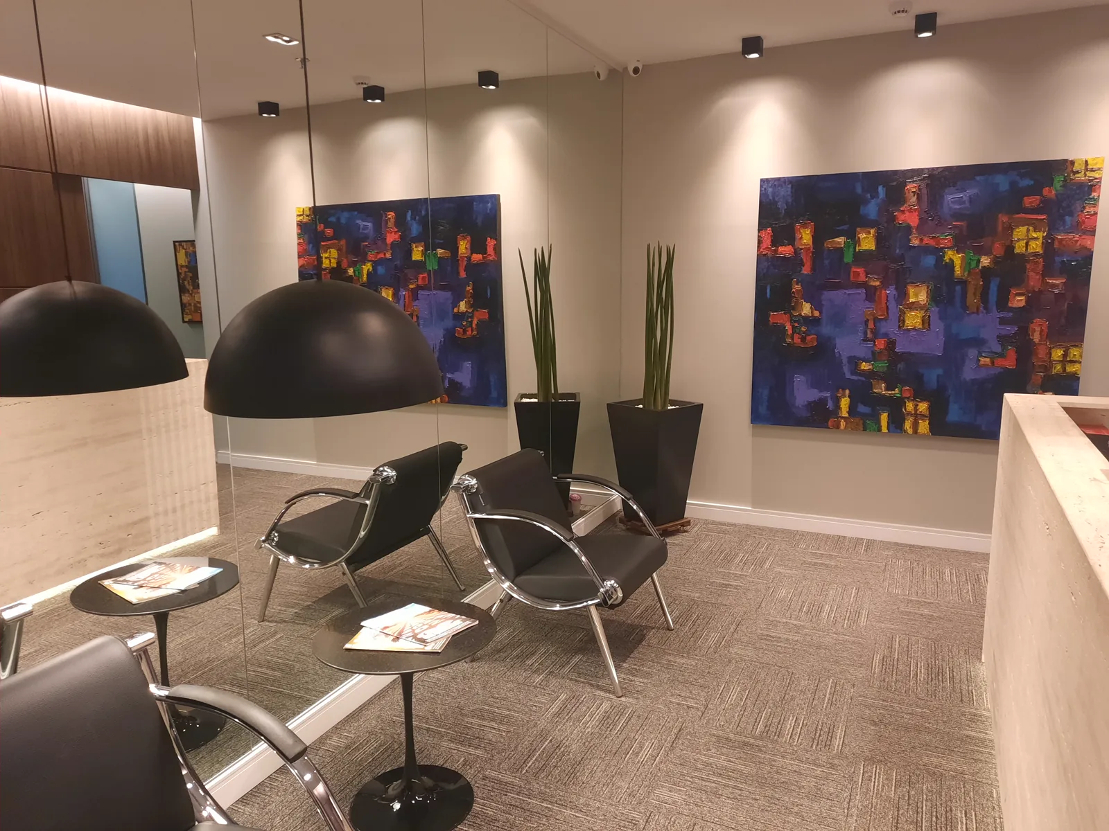 Sala de espera do escritório, com poltronas, mesas de apoio e quadros na parede