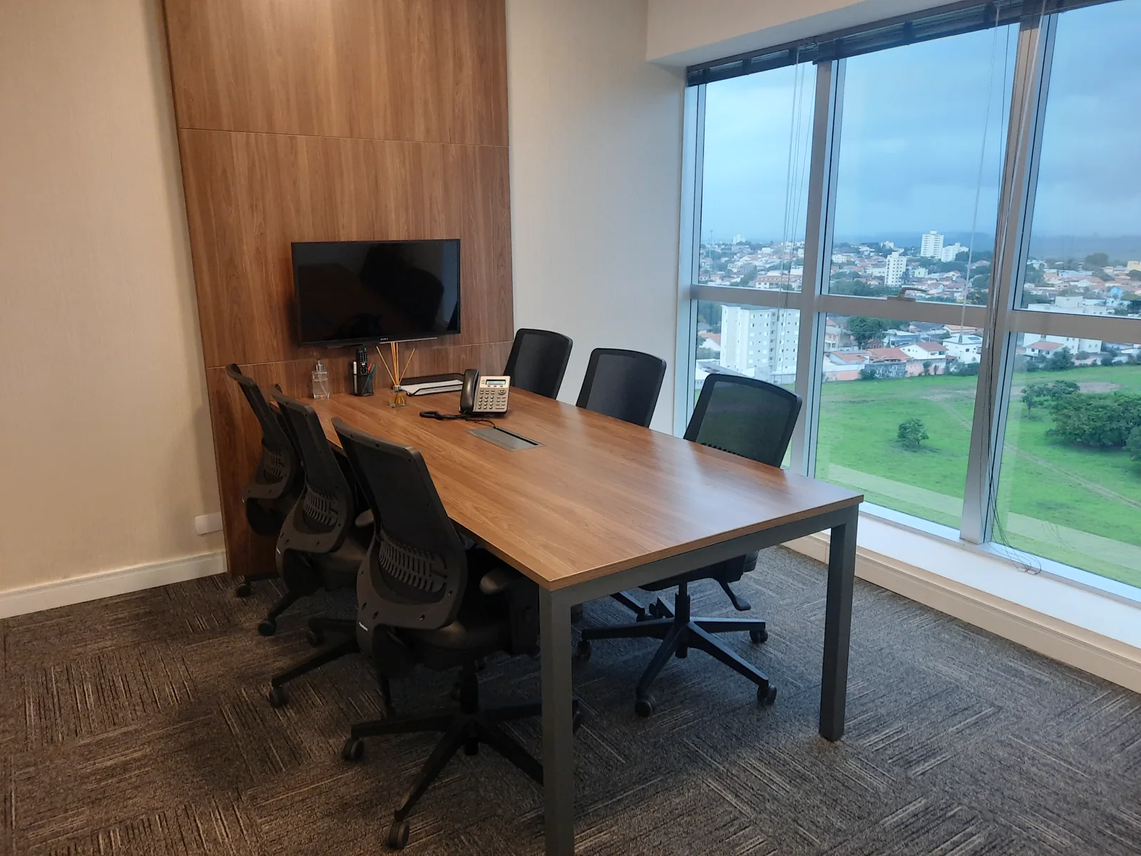 Sala de reunião menor, com televisor e painel de madeira